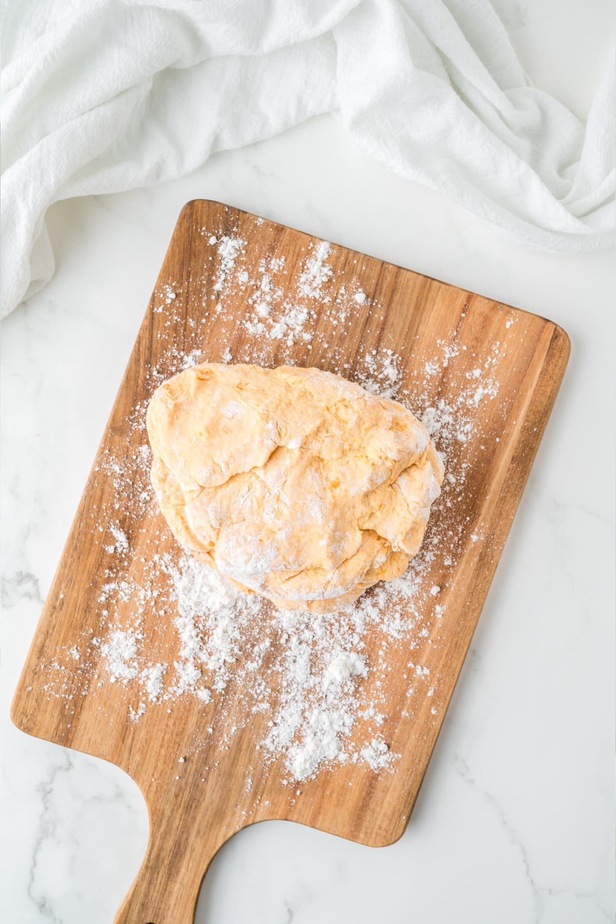 A ball of raw, orange-tinted dough on a wooden cutting board dusted with flour.