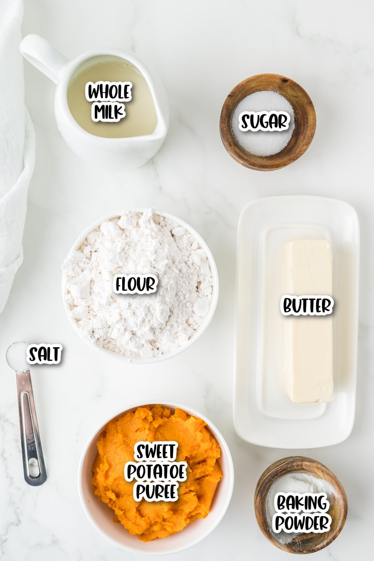 Ingredients for a recipe: whole milk, sugar, flour, butter, salt, sweet potato puree, and baking powder arranged on a white surface.