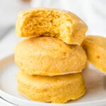 A stack of three orange-hued biscuits on a white plate, with a bite taken out of the top one.